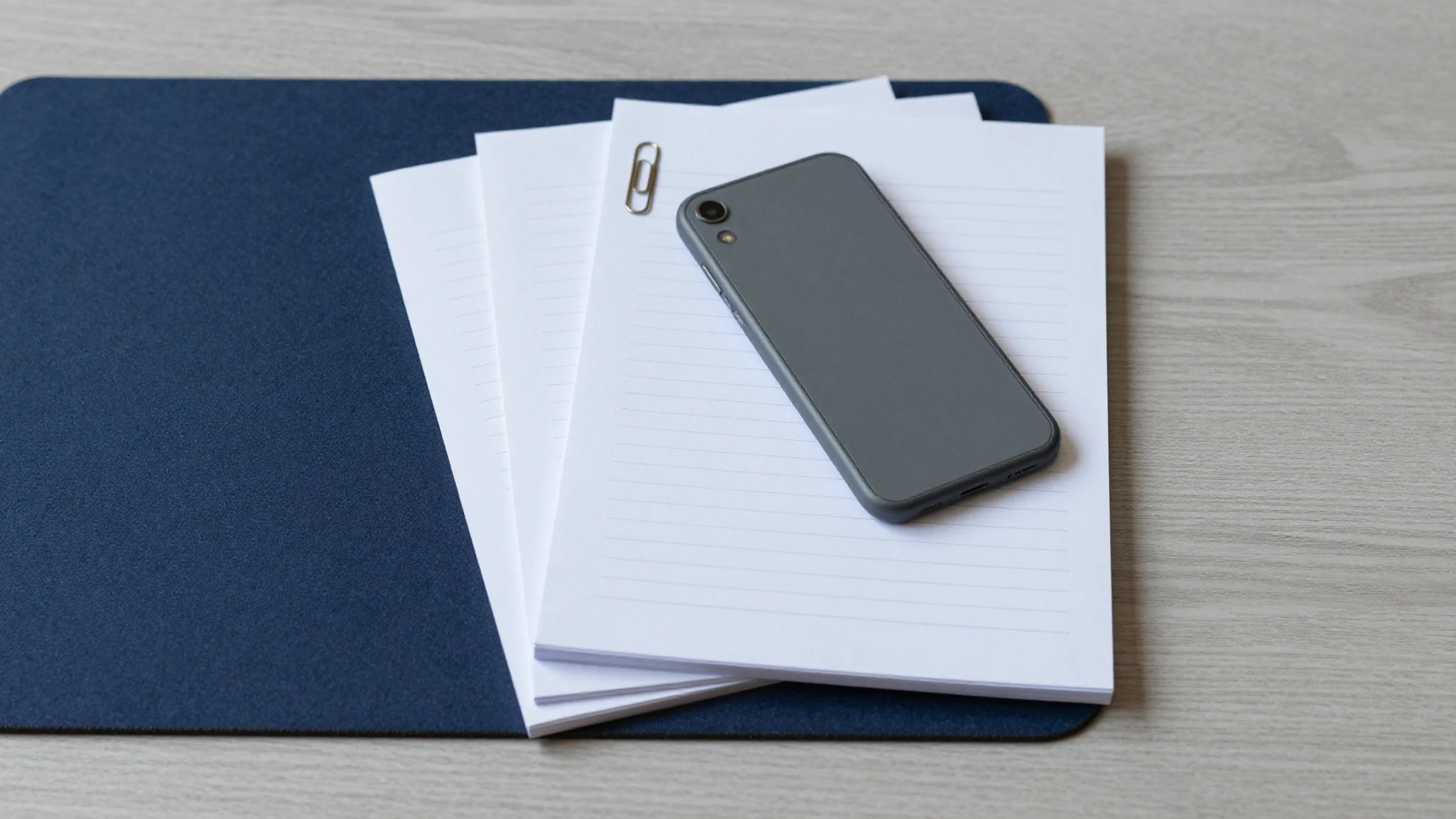 Illustration: a loose stack of ruled paper on a desk, with a phone lying face down on top and a paperclip on the top sheet.